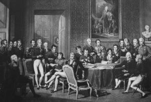 Delegierte des Wiener Kongresses, zeitgenössischer Kupferstich von Jean Godefroy nach einem Gemälde von Jean-Baptiste Isabey. In der linken Bildhälfte im Vordergrund stehend: Fürst Klemens Wenzel von Metternich.